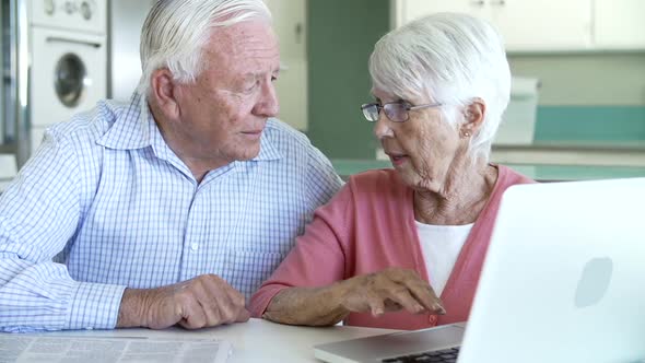 Senior Couple Using Laptop At Home In Kitchen