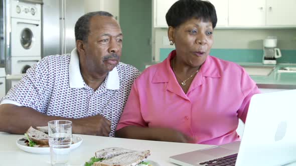 Senior Couple Using Laptop At Home Whilst Having Lunch