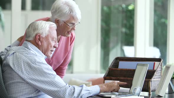 Senior Couple Using Laptop On Desk At Home