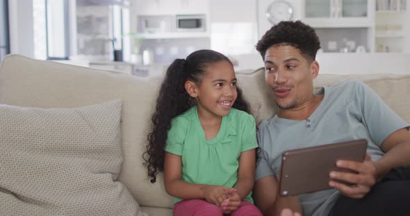 Happy biracial father and daughter sitting on sofa using tablet
