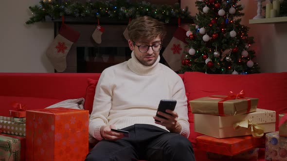 Young caucasian man with a phone and credit card Christmas buying online.