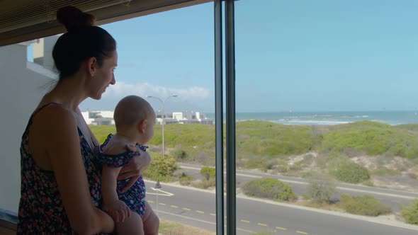 Mother Holding Baby Near a Window Showing the Ocean To the Child