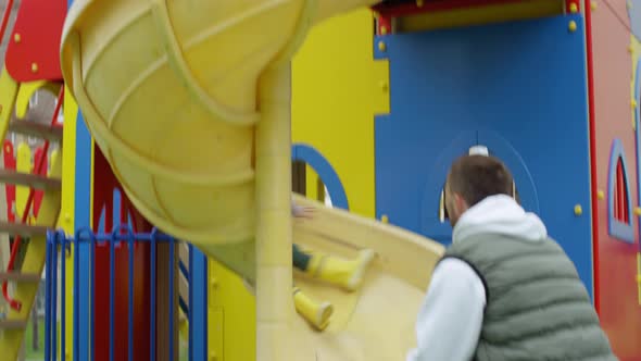 Happy Caucasian Boy Having Fun on Playground Slide with Parents