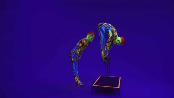 Acrobats In Luminous Ultraviolet Suits Do Racks And Transverse Splits, Body Art Glows In Darkness