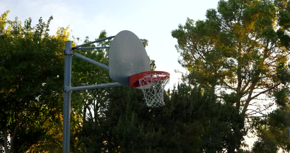 Panning from a basketball hoop with metal backboard and and orange rim to the empty concrete park co