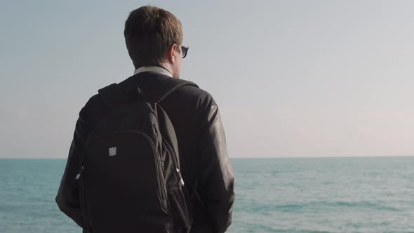 Man Stands Near the Sea with a Backpack on His Back and Looks Into the Distance