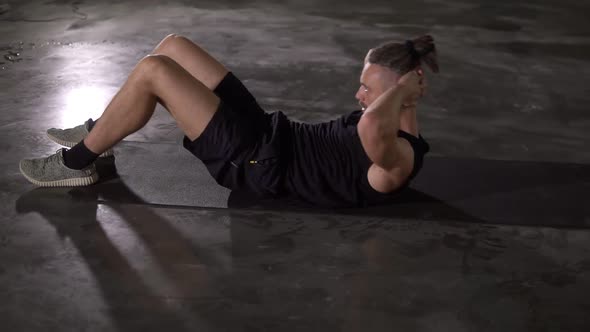 Muscular Man in Sportswear Making Abdominal Sport Exercise on Fitness Mat Using Alone in Loft Studio