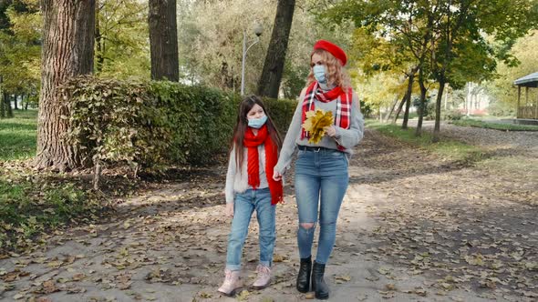 Young Mother and Her Daughter in Masks Walking Together in an Autumn Park