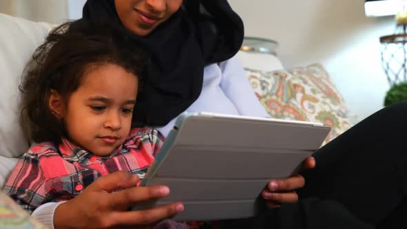 Young mother using a digital tablet with her daughter on the sofa at home 4k