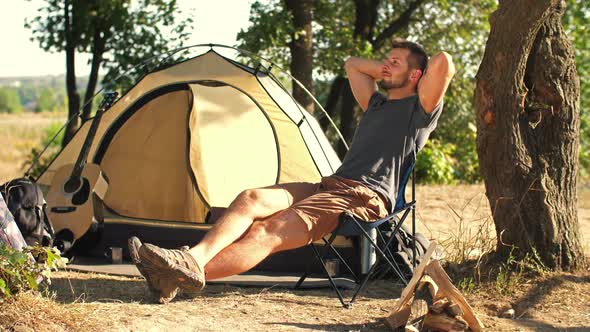 Man Tourist Resting on Chair in Front of Tent