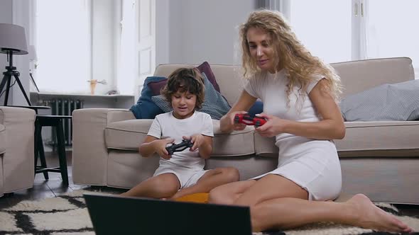  Woman Sitting Together with Her Cute Son on the Floor Enjoying the Play of Video Game 