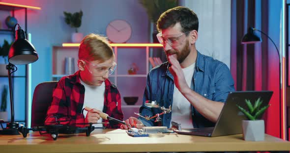 Father and His Son in Glasses Soldering Together at Home in the Evening and Giving High Five