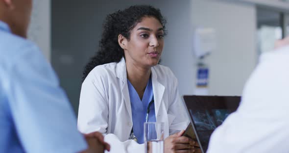 Asian female doctor wearing lab coat sitting and addressing hospital colleagues at a meeting