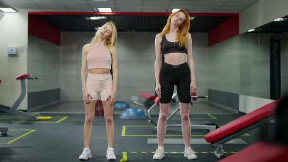 Wide Shot of Slim Blond and Redhead Young Women Warming Up in Gym Indoors