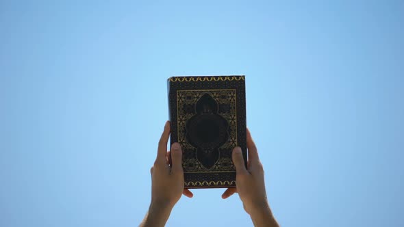 Male Hands Raising Koran to Sky, Sharing Sacramental Islamic Teachings, Faith