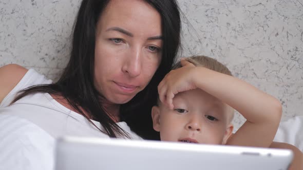 Young Beautiful Mother and Her Cute Son Makes Online Shopping on a Tablet and Smiling While Lying on