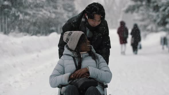 Couple of Asian Guy and His Black Girlfriend in the Wheelchair Walking in Winter Park