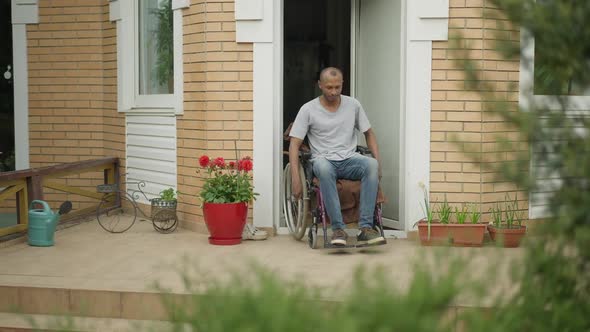 Paralyzed African American Man Riding Wheelchair on Backyard Porch Outdoors