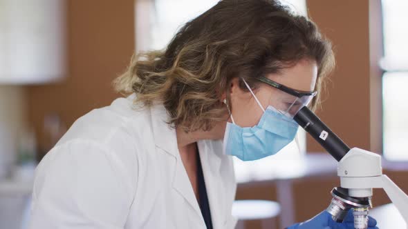 Female teacher wearing face mask and protective glasses using microscope in laboratory