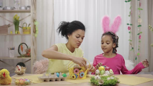 Mom and Daughter with Funny Bunny Ears Putting Easter Cake and Colored Eggs in Basket