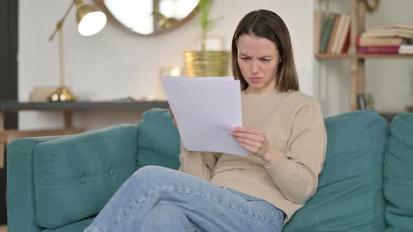 Young Woman with Documents Reacting To Loss on Sofa 