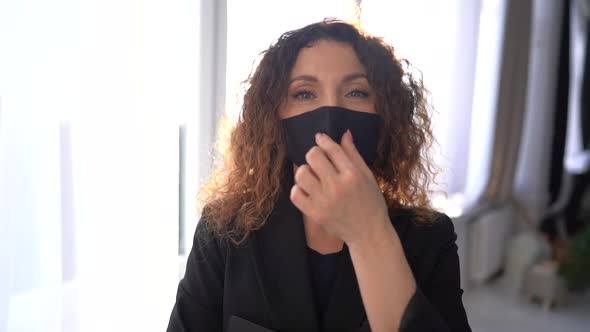 Sunny Indoor Portrait of a Lovely Curlyhaired Business Woman in a Black Mask with a Folder in Her