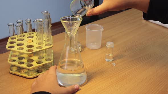 Pupil's Hands Closeup Pouring a Chemical Reagent From a Glass Into a Flask