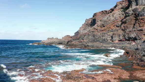 Aerial dolly pull back over ocean coastline close to big basalt stone