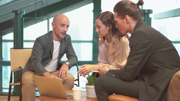 Creative business team of three people discussing business plan while sitting at table in office