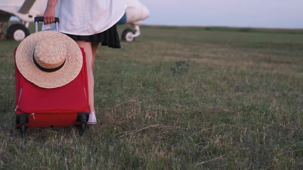 A Girl Is Carrying a Suitcase To the Plane Across the Field Closeup