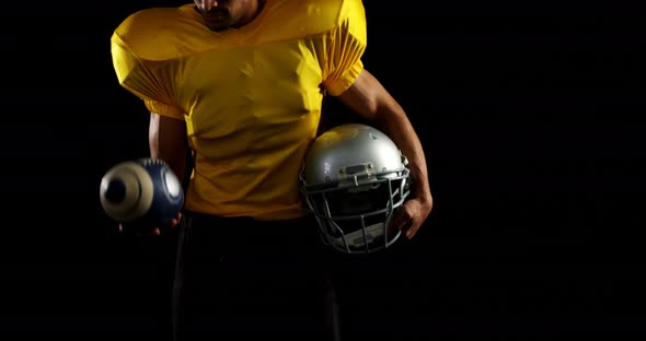 American football player holding head gear and juggling ball