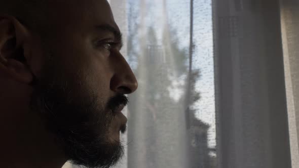 Minority Asian Male Looking Out Of Window In Pensive Mood During Locked Down. Locked Off, Side View,