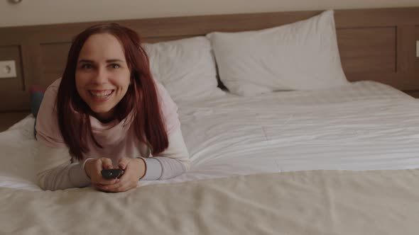 Young Woman Lying on Bed Watching Tv and Laughing