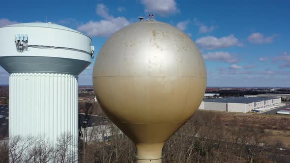 An aerial shot orbiting a silver water tower with another blue one in the background. The drone came
