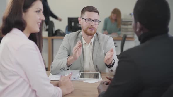 Young Caucasian Manager with Red Beard Advicing Young Biracial Couple on the Buying of New