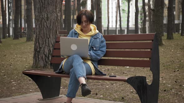 Young attractive woman freelancer is working on laptop computer outdoor in city park