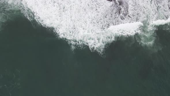 Top down aerial view of giant ocean waves crashing and foaming in coral beach