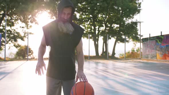 Stylish Middle Aged Man with Long Gray Bearded Playing Basketball During Sunset