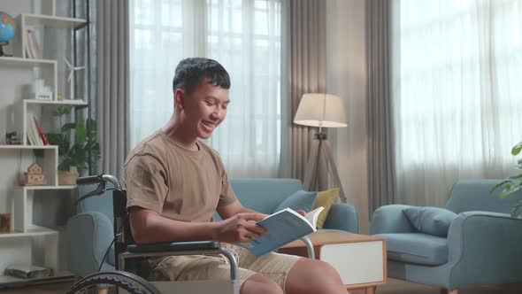 Young Asian Boy Sitting In A Wheelchair And Reading Book At Home
