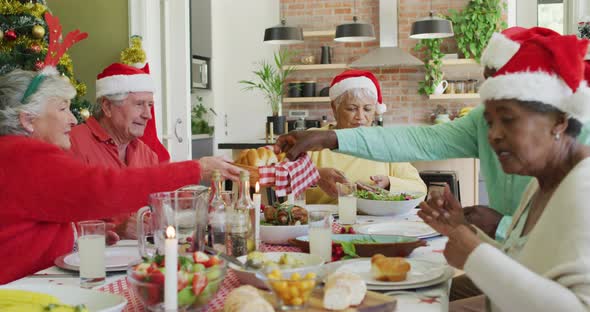 Group of happy diverse senior friends in santa hats making a toast at christmas dinner table at home