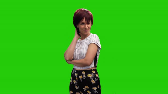 Cheerful short haired brunette female adjusting hair on green screen