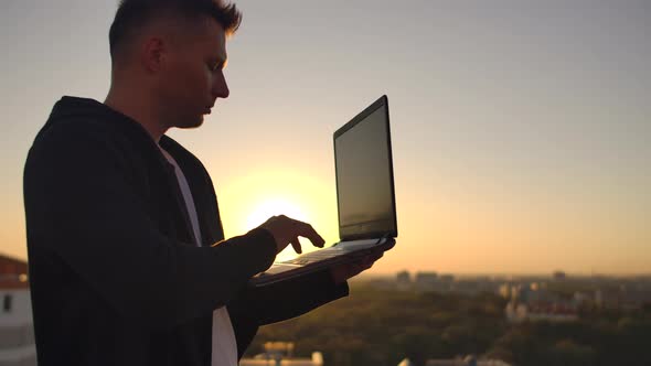 Hacker Using Laptop on Rooftop with City View and Forex Chart. Hacking and Stats Concept