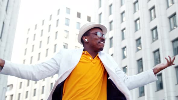 Joyful black man in wireless headphones and chameleon glasses sings on street