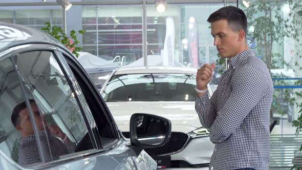 Young Man Rubbing His Chin Thoughtfully, Choosing New Car To Buy at Dealership