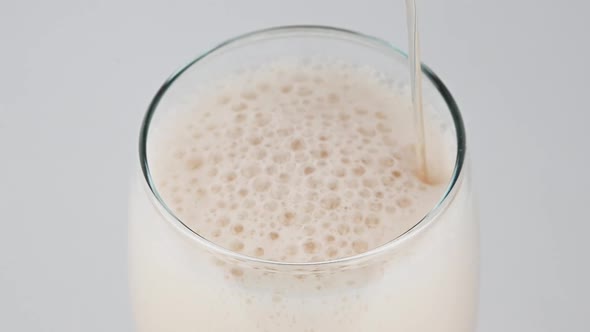 Pouring lager beer with bubbles and froth over the top in glass over white background