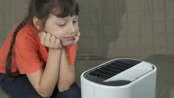 Child and air purifier. Cute little girl breath by air purifier in room. 