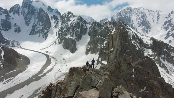 Two Climbers on Peak of Rock. Snow-Capped Mountains. Aerial View