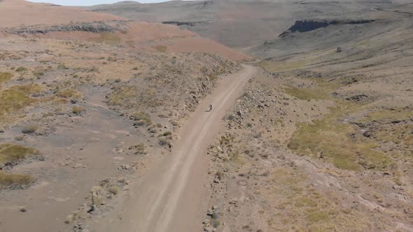 aerial shot following a mountain biker climbing up a pass on a gravel road