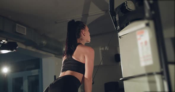 Rear View of Strong Female Athlete Pulls Bar with Rope on Fitness Machine