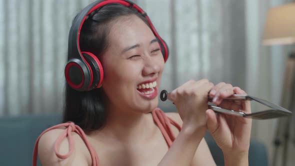 Smiling Asian Woman Listening To Music With Headphones And Singing While Slicing The Cucumber